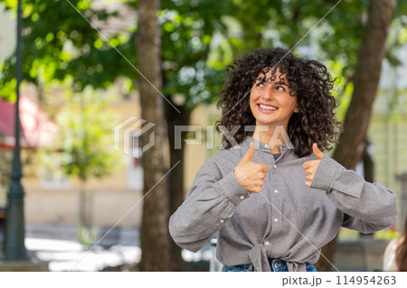 Happy young woman girl showing thumbs up like sign something good positive feedback on city street Happy young woman girl showing thumbs up like sign something good positive feedback on city street 114954263