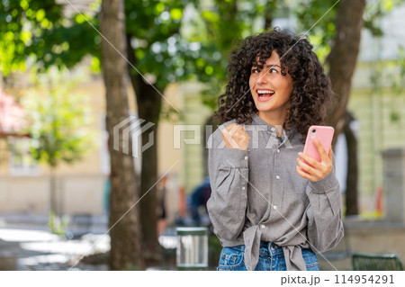 Caucasian woman use mobile smartphone celebrating win good message news outdoors on city street 114954291