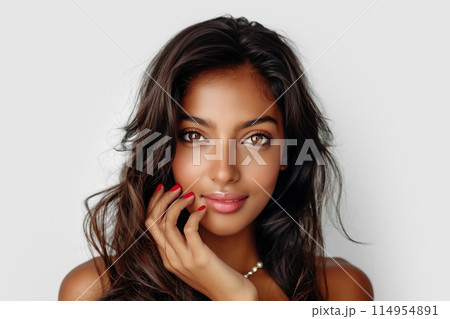 Smiling young woman with dark hair and a pearl necklace, gently touching her face 114954891