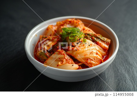 Bowl of kimchi on a dark slate background, vibrant red hues 114955008