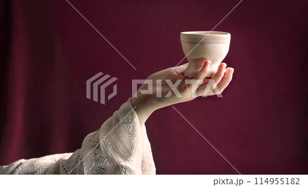 A hand in ancient clothing holds a clay bowl 114955182