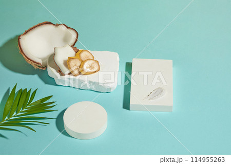 Overhead photograph on blue background with a few flat lay white blank pedestals in different shaped, coconut and banana decorated above. Product presentation space and blank space for adding text 114955263