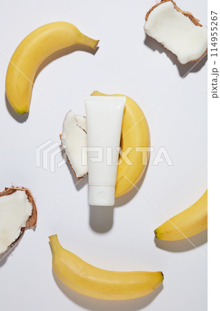 The white unbranded cosmetic tube flat lay on a white counter top, with various pieces of coconut and a bananas lay scattered around. Photo for promotion with overhead view and blank space for design 114955267