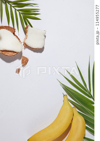 Tropical fruit as banana and coconut featured on white countertop, decorated by fresh green coconut leaves, vacant space in center for displaying product has fruit origin. Top view, copy space Tropical fruit as banana and coconut featured on white countertop, decorated by fresh green coconut leaves, vacant space in center for displaying product has fruit origin. Top view, copy space 114955277