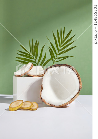Photo was taken from front view on green background, a rectangular platform containing some pieces of coconut, next to a half of coconut and some banana slices, green coconut leaves decorated in back Photo was taken from front view on green background, a rectangular platform containing some pieces of coconut, next to a half of coconut and some banana slices, green coconut leaves decorated in back 114955301