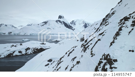 Fly over mountain snow covered rock in Antarctica. Arctic slope hill over cold polar ocean, mountain range peak in background. Harsh extreme low temperature conditions. South Pole explore and travel Fly over mountain snow covered rock in Antarctica. Arctic slope hill over cold polar ocean, mountain range peak in background. Harsh extreme low temperature conditions. South Pole explore and travel 114955747