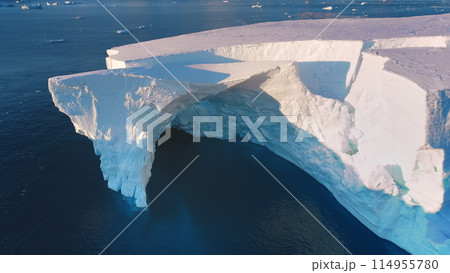 Massive iceberg drifts sunset polar ocean. Giant crashed glacier arch cave in Antarctica. Huge ice wall in pink evening light. Arctic frozen ocean landscape. Travel. Aerial top view drone flight 114955780