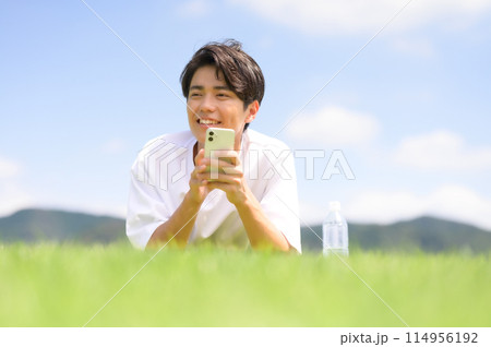芝生にうつ伏せでスマホを見る男性 114956192