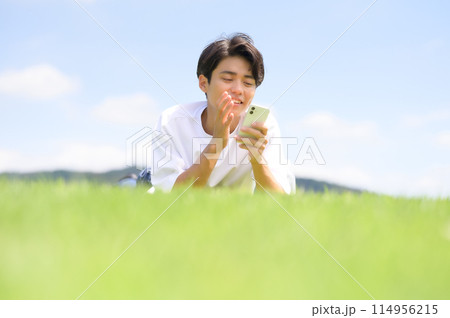 芝生にうつ伏せでスマホを見る男性 114956215