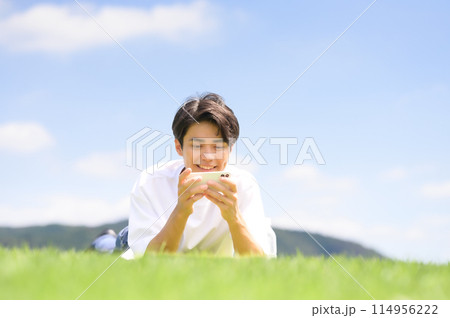 芝生にうつ伏せでスマホを見る男性 114956222