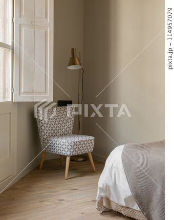 Cozy bedroom corner with patterned chair, modern floor lamp, and neutral tones Cozy bedroom corner with patterned chair, modern floor lamp, and neutral tones 114957079