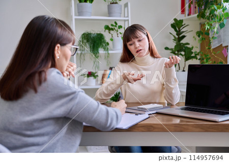 Sad teenage girl talking to psychotherapist at therapy session in office Sad teenage girl talking to psychotherapist at therapy session in office 114957694