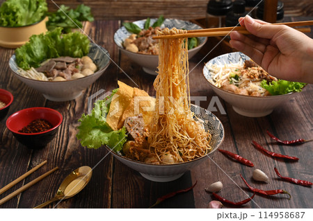 Hand using chopsticks to picking up tasty spicy egg noodles from bowl. Thai noodles and Asian food concept 114958687