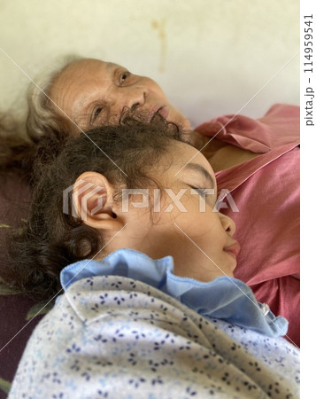 Asian senior woman with her little daughter lying on a sofa in her room 114959541