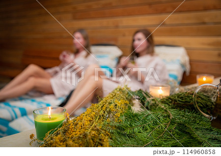 Two women relaxing in a sauna surrounded by candles and herbs Two women relaxing in a sauna surrounded by candles and herbs 114960858