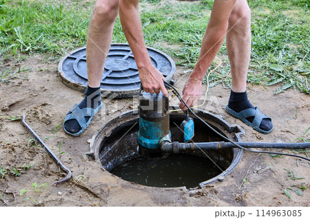 Plumber submerges wastewater pump into septic tank effluent to pumping sewage water before tank maintenance. 114963085