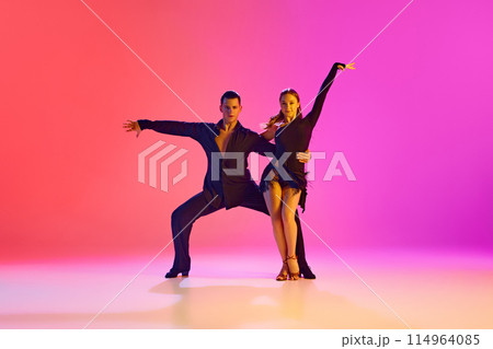 Ballroom dance duo, dressed black stages costumes in action in neon lighting against vibrant gradient background. Ballroom dance duo, dressed black stages costumes in action in neon lighting against vibrant gradient background. 114964085