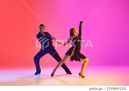 Portrait of young talented couple practicing ballroom dancing in motion in neon lighting against vibrant gradient background. Portrait of young talented couple practicing ballroom dancing in motion in neon lighting against vibrant gradient background. 114964120