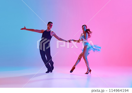 Dynamic shot of young man and woman dancing Cha Cha in motion in neon lighting against gradient background. Dynamic shot of young man and woman dancing Cha Cha in motion in neon lighting against gradient background. 114964194