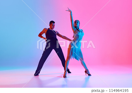 Art in Motion. Two young people, man and woman, ballroom dancers display their skills in neon lighting against gradient background. Art in Motion. Two young people, man and woman, ballroom dancers display their skills in neon lighting against gradient background. 114964195