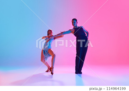 Ballroom dancers, man and woman in fashion stage costumes strike graceful pose in neon lighting against gradient background. 114964199
