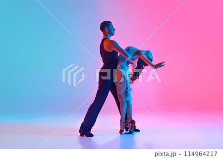 Pair of dancers embody art of ballroom dance, perform their refined movements in neon lighting against gradient background. Pair of dancers embody art of ballroom dance, perform their refined movements in neon lighting against gradient background. 114964217