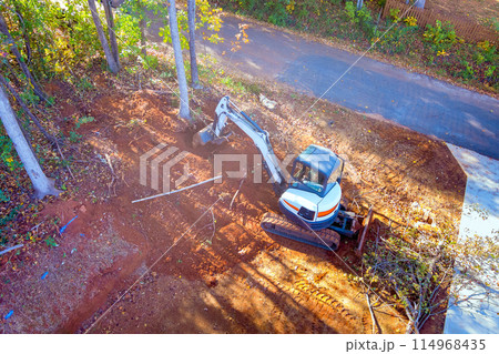 Tractor uproots trees during construction in order to clear land for building Tractor uproots trees during construction in order to clear land for building 114968435
