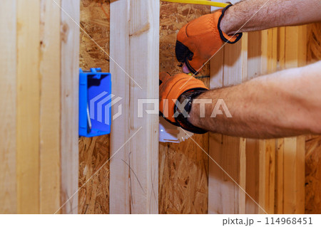 An electrician connects wires to socket box in new building during construction 114968451