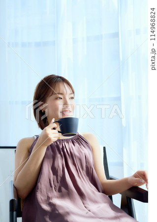 部屋の中で椅子に座ってコーヒーを飲む女性 114968824