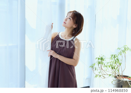 部屋の中でレースカーテン越しにくつろぐ女性 114968850