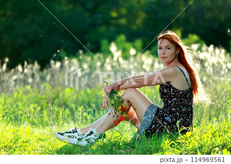 A girl with wild poppies enjoys the view from a hill near the river. Joy, happiness, serenity. Wild poppies by the river. 114969561