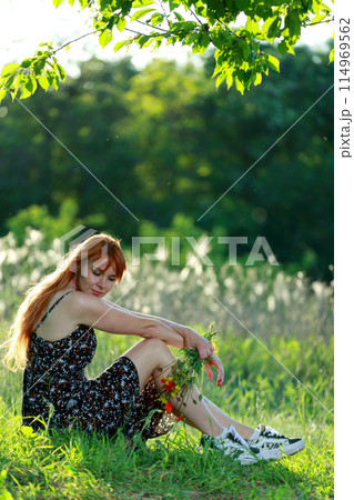 A girl with wild poppies enjoys the view from a hill near the river. Joy, happiness, serenity. Wild poppies by the river. 114969562