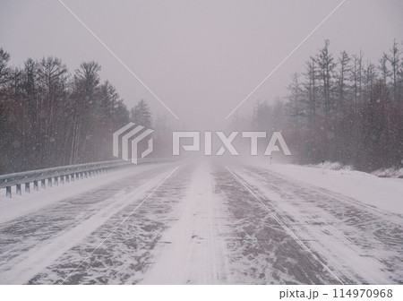 Snow-covered highway through forest during intense winter storm in daytime Snow-covered highway through forest during intense winter storm in daytime 114970968
