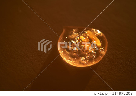 Drop of serum shimmering in the sun on a beige background. Drop of serum shimmering in the sun on a beige background. 114972208