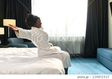 Side view portrait of young Black woman falling onto bed enjoying relaxing SPA vacation in hotel, copy space Side view portrait of young Black woman falling onto bed enjoying relaxing SPA vacation in hotel, copy space 114972317