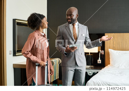 Portrait of luxury hotel manager welcoming young Black woman entering hotel room enjoying travel copy space Portrait of luxury hotel manager welcoming young Black woman entering hotel room enjoying travel copy space 114972425
