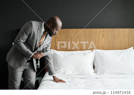 Minimal side view portrait of Black man as hotel manager inspecting hotel room with fresh white bed sheets copy space 114972438