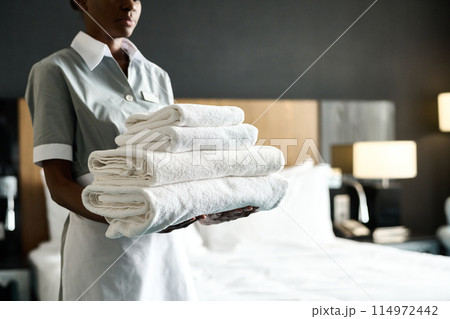 Cropped shot of young African American woman as housekeeper holding stack of fresh bedding preparing room in luxury hotel copy space Cropped shot of young African American woman as housekeeper holding stack of fresh bedding preparing room in luxury hotel copy space 114972442