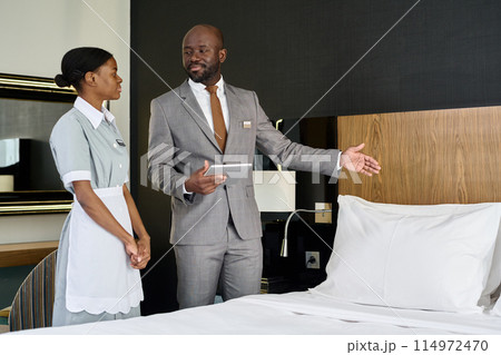 Portrait of smiling Black man training housekeeper and inspecting work in hotel room copy space Portrait of smiling Black man training housekeeper and inspecting work in hotel room copy space 114972470