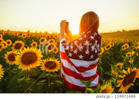 Beautiful girl with the American flag in a sunflower field. 4th of July. Fourth of July. Freedom. 114972498