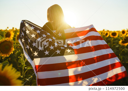 Beautiful girl with the American flag in a sunflower field. 4th of July. Fourth of July. Freedom. 114972500