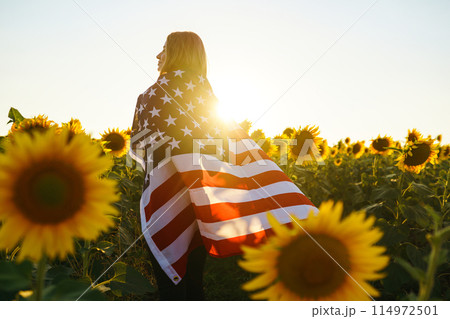 Beautiful girl with the American flag in a sunflower field. 4th of July. Fourth of July. Freedom. 114972501