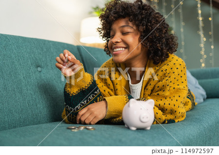 Saving money investment for future. African American girl putting money coin in pink piggy bank. Saving investment budget business wealth retirement financial money banking concept 114972597