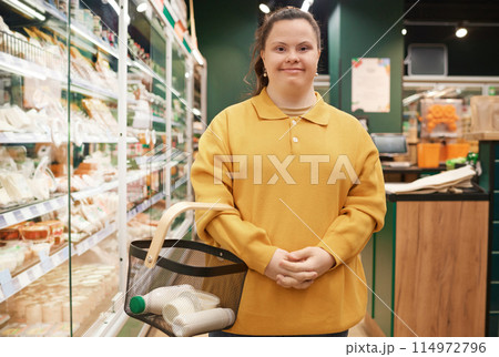 Waist up portrait of cheerful young woman with Down syndrome smiling at camera in supermarket while buying groceries 114972796