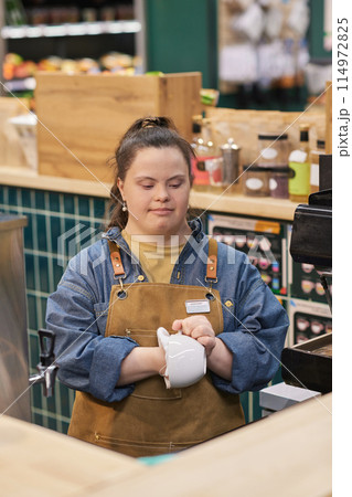 Vertical portrait of young woman with disability working in cafe and cleaning coffee cups enjoying occupational training 114972825