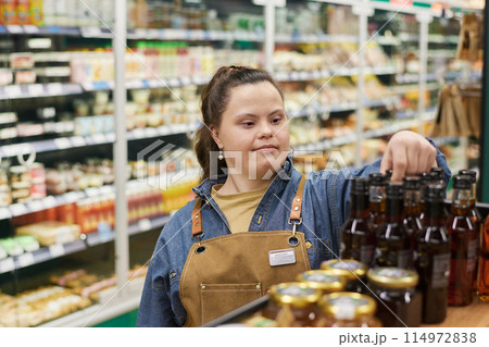 Waist up portrait of adult woman with Down syndrome working in supermarket and reviewing shelf stock Waist up portrait of adult woman with Down syndrome working in supermarket and reviewing shelf stock 114972838