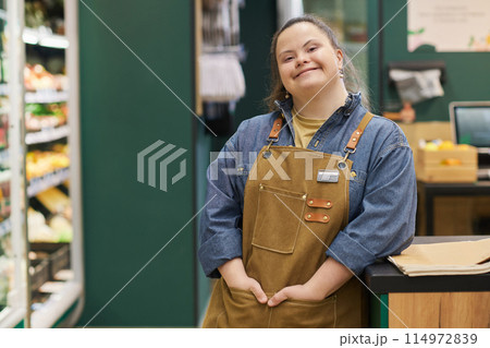 Waist up portrait of smiling young woman with Down syndrome enjoying work in supermarket and looking at camera with happiness copy space Waist up portrait of smiling young woman with Down syndrome enjoying work in supermarket and looking at camera with happiness copy space 114972839