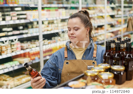 Waist up portrait of smiling young woman with Down syndrome working in supermarket and inspecting stock on shelves copy space 114972840