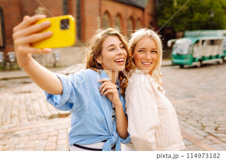 Happy women taking selfie while walking down street. Fashion, travel, technology, blogging concept. Happy women taking selfie while walking down street. Fashion, travel, technology, blogging concept. 114973182