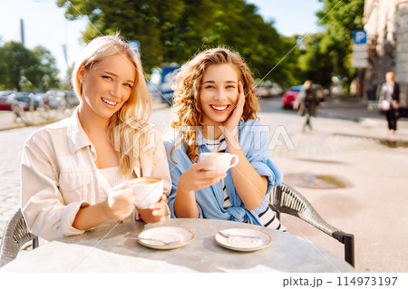 Portrait of a smiling young women friends sitting outdoors in cafe drinking coffee. Beauty, relax. 114973197